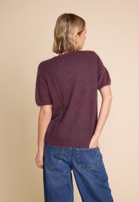 Kortermet, bløt lilla genser i en lodden materiale, med en avslappet passform og ribbestrikket kant, sammen med høyhåndte blå jeans.