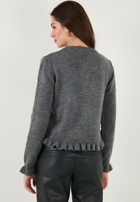 Maglione grigio a maglia con orlo e polsini arricciati, dotato di un collo rotondo e una finitura morbida e testurizzata. Indossato con pantaloni in pelle neri.