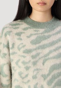 Maglione lavorato a maglia in beige chiaro e verde con una texture morbida e pelosa, caratterizzato da un delicato motivo a stampa animale e un colletto a girocollo a coste.
