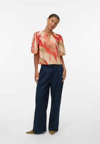 Chemisier à manches courtes en tissu texturé avec une base beige et de vifs motifs abstraits rouges et roses ; assorti à un pantalon large marine.