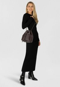 Czarna sukienka z długim rękawem, do kostek, w połączeniu z czarnymi szpilkami. Brązowa skórzana torba w kształcie wiadra z zaciąganym zapięciem, zdobiona subtelnymi wzorami.
