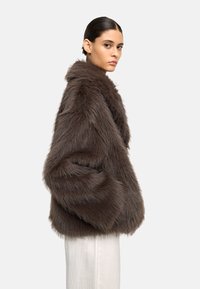 Brązowa kurtka z futra sztucznego z wysokim kołnierzem i luźnym krojem. Posiada teksturowaną powierzchnię, długie rękawy oraz boczne kieszenie.