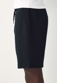 Dark blue patterned shorts with a textured geometric design, featuring side pockets and a drawstring waist. Material is soft and flexible.