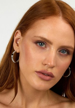 Orecchini a cerchio argentati con gemme trasparenti, caratterizzati da una texture liscia e una forma rotonda, abbinati a un trucco naturale.