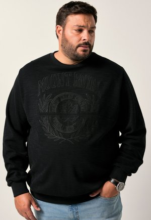Sudadera negra con un acabado texturizado y un logo en relieve "MOUNT ROYAL". Presenta puños y dobladillo acanalados, combinada con jeans de color azul claro.