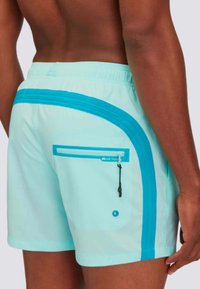 Pantaloni da bagno azzurri con un accento turchese a contrasto. Presentano una tasca posteriore con zip e un cordoncino in vita.