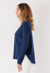 Maglietta a maniche lunghe di colore blu navy realizzata in tessuto morbido, caratterizzata da una vestibilità comoda e spacco laterale. Texture liscia con una leggera lucentezza.