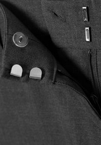 Tissu noir à texture lisse avec une poche équipée d'un bouton transparent et d'accents métalliques, incluant une fermeture éclair et des clips.