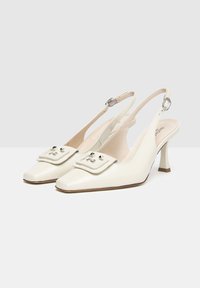 Tacchi slingback bianchi in vernice con punta quadrata e un distintivo fibbia decorativa con elementi metallici. Altezza del tacco di 7,5 cm.