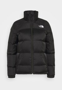 Doudoune noire avec un col haut, fermeture éclair et poignets côtelés. Elle présente des sections matelassées et un logo sur la poitrine gauche.