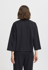 Pullover nero, di taglio loose-fit, con maniche a tre quarti. Realizzato in tessuto morbido, presenta un colletto rotondo e un design minimalista.