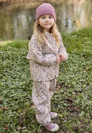 Chaqueta y pantalones acolchados con estampado floral en color crema con detalles en burdeos. Gorro de punto rosa con canalé y zapatos rosa claro. Entorno natural al aire libre.