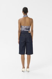 Denim bermudashorts med fem lommer, midjehøyde, og en beige lærmerke bak; kombinert med en mønstrete halterneck-top.
