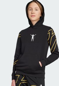 Felpa nera con cappuccio e tasca frontale, caratterizzata da strisce diagonali gialle sulle maniche e una grafica bianca di una figura con le braccia sollevate.