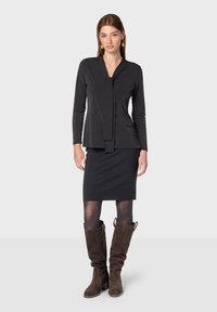 Černý dlouhý rukáv top s detailem na zavázání, zkombinovaný s černou tužkovou sukní a hnědými semišovými vysokými botami. Hladká textura, přiléhavý střih.