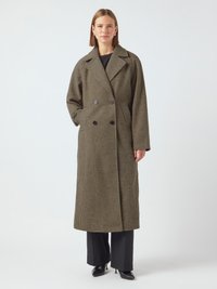 Cappotto lungo doppiopetto in motivo houndstooth marrone, con colletto areato e tasche laterali, abbinato a pantaloni neri e tacchi.