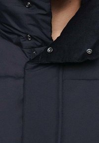 Czarna pikowana kurtka z wysokim kołnierzem, zapinana na zatrzaski, z teksturowanym akcentem na kołnierzu. Gładki materiał z przeszywanym wzorem.