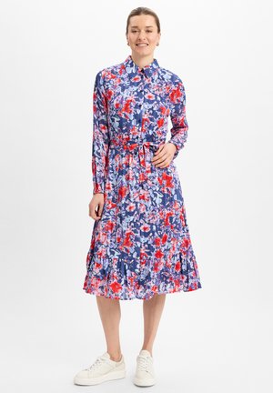 Blumenkleid mit langen Ärmeln, einem kragenlosen Ausschnitt und einem taillierten Bund. Es hat ein Muster in Blau, Rot und Weiß mit einem volantsaum.