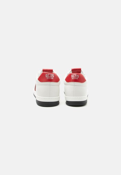 Ζευγάρι λευκά αθλητικά παπούτσια με κόκκινες ταμπελίτσες στη φτέρνα που φέρουν το λευκό κείμενο "GCDS XCIV 1988", φωτογραφημένα από πίσω σε απλό ανοιχτόφωτο φόντο.