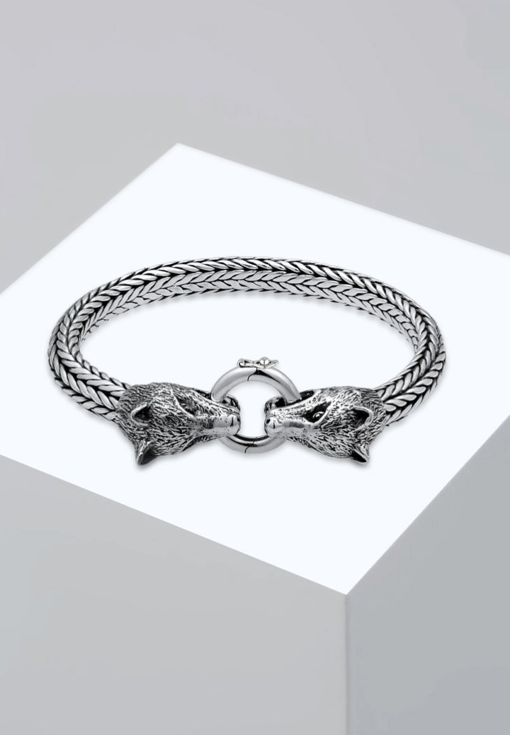 Silverflätat armband med två varghuvuden som lås och en cirkulär ringstängning. Texturerade detaljer förbättrar designen.