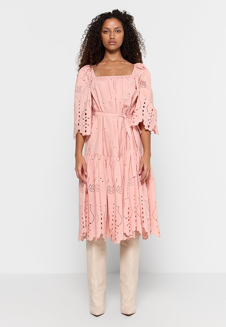 Rosa Baumwollenkleid mit A-Linien-Silhouette, Augenlet-Details, Puffärmeln und einem gegürtelten Taillenbereich, kombiniert mit knielangen beigen Stiefeln.