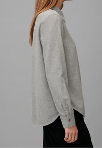Lichtgrijze langemouwen shirt van een zachte, textuurstof. Bevat een kraag met knoopsluiting en een ronde zoom met knoopmanchetten.