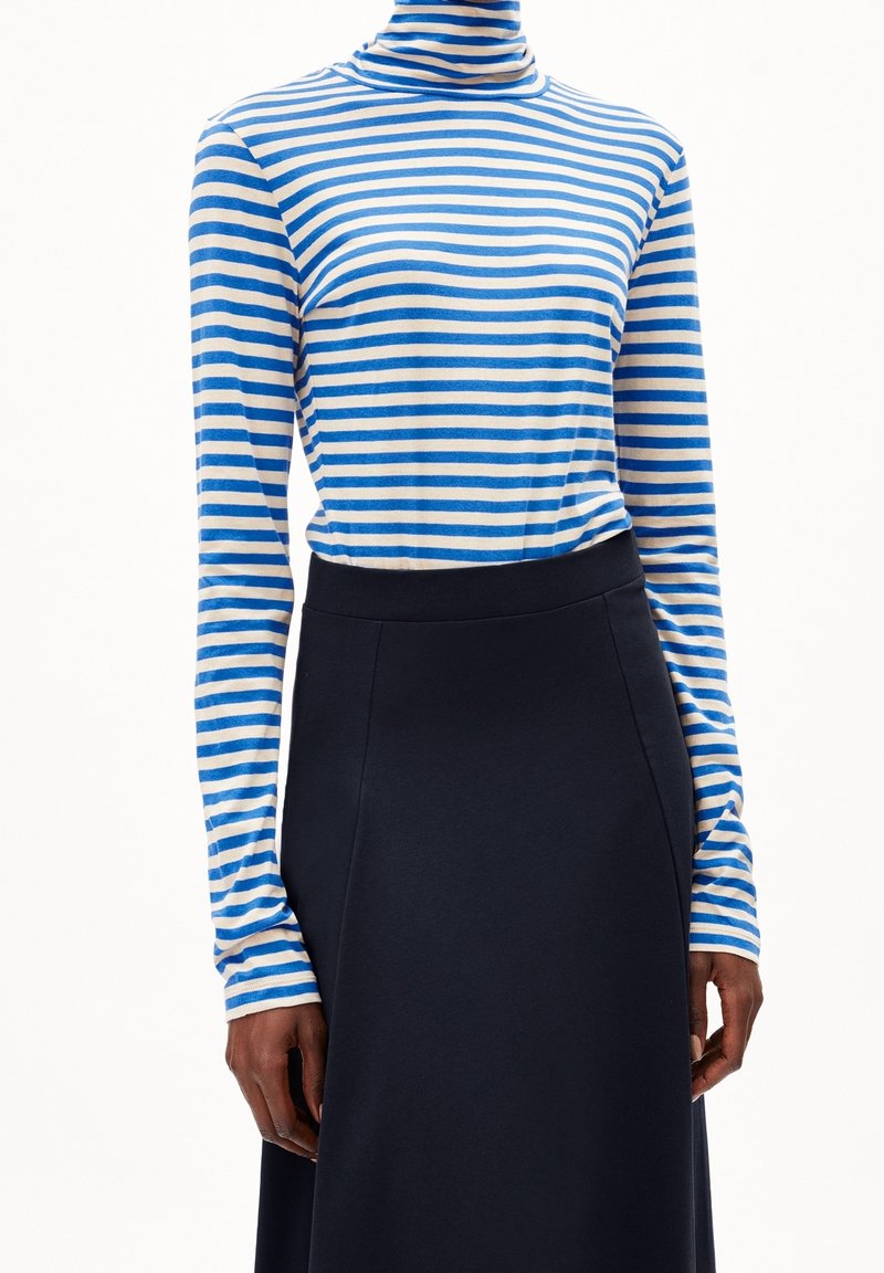 Haut col montant rayé en bleu clair et crème, associé à une jupe unie bleu marine foncé ; les deux vêtements ont une texture lisse et une silhouette ajustée.