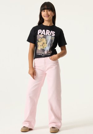 Zwart T-shirt met "PARIS" print en bloemmotief, gecombineerd met lichtroze wijde jeans en beige sneakers.