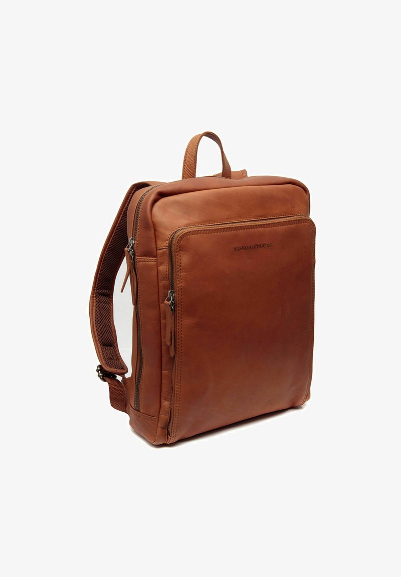 Mochila de cuero marrón con forma rectangular, que presenta un bolsillo frontal, un asa superior y correas acolchadas. Textura suave, diseño minimalista.