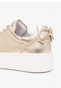 Goldene Ledersneaker mit weißer Sohle, ausgestattet mit einer Schleifenakzent am Absatz und metallischem Finish. Strukturiertes Oberflächendesign.
