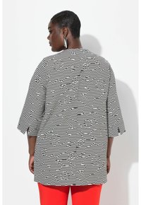Tunic a righe bianche e nere con motivo floreale, vestibilità ampia, maniche a tre quarti e orlo dritto, abbinata a pantaloni rossi.