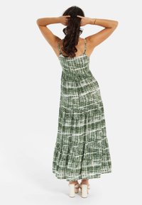 Green and white tie-dye maxi dress with spaghetti straps, ruched bodice, tiered skirt, and a lightweight fabric. Accented with simple heels.