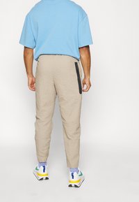 Beige byxor med textur och avsmalnande passform samt en svart zip-ficka på sidan, matchade med en ljusblå t-shirt och färgglada sneakers.