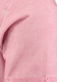 Camicia in cotone rosa tenue con texture a coste, caratterizzata da una cucitura laterale e un orlo piegato. Design semplice senza motivi aggiuntivi o accessori.