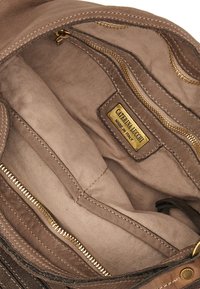 La borsa a mano in pelle color tan presenta un interno con diverse tasche e cerniere in tonalità oro. Etichetta del marchio visibile, con una sottile texture del tessuto. Design spazioso.