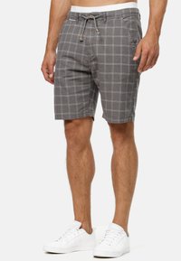 Shorts gris à carreaux en coton, dotés d'une taille à cordon de serrage avec des accents noir et blanc. Tenue associée à des baskets blanches.