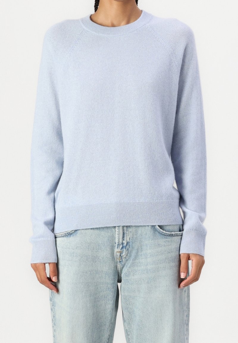 Suéter de lana azul claro con cuello redondo, mangas raglán y puños y dobladillo acanalados, combinado con jeans de denim claros.