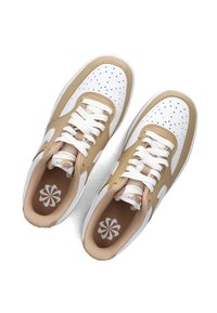 Bruine en witte sneakers met een geperforeerd ontwerp, witte veters en een beige gaasvoering. Heeft een logo op de tong en een patroon op de binnenzool.