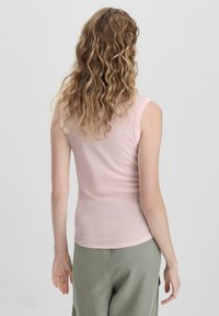 Lichtroze mouwloze top, aansluitend ontwerp, zachte stof, gladde textuur. Gecombineerd met losjes zittende groene broek, minimaal zichtbare details.