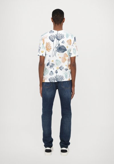 Short-sleeved white t-shirt with colorful floral pattern, paired with dark blue jeans and black-and-white sneakers.