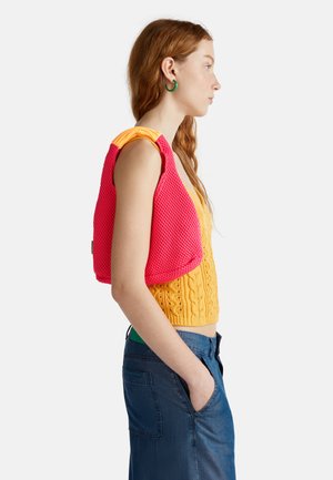 Knit crop top in yellow with cable pattern and pink mesh accents. Mid-length with wide straps. Pair with blue denim skirt.