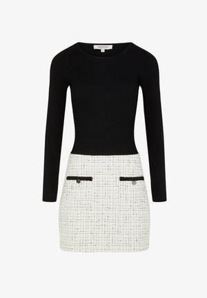 Sort ribbet top med lange ærmer, som overgår til en hvid struktureret nederdel med sorte akcentlommer og sølvknapper.