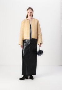 Veste cropped en cuir jaune avec un col rond, associée à une jupe maxi en cuir noire et des bottines à talons noires. Sac pochette noir.