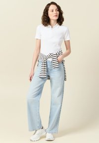 Polo blanco de canalé con mangas cortas, combinado con unos vaqueros de pierna ancha de color azul claro. Top a rayas en blanco y negro anudado a la cintura, zapatillas blancas.