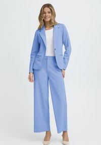 Svetlo modro obleko, ki vsebuje prilagojeni blazer z dvema sprednjima žepoma in hlače z širokimi hlačnicami. Oblečeno preko belega topa in kombinirano z bež visokimi petami.