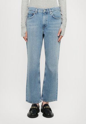 Light blue denim wide-leg jeans feature a mid-rise waist, five-pocket design, and raw hem. Paired with black loafers.