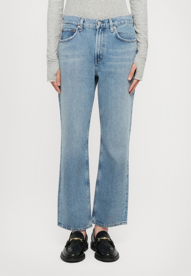 Light blue denim wide-leg jeans feature a mid-rise waist, five-pocket design, and raw hem. Paired with black loafers.