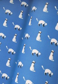 Tkanina z powtarzającym się wzorem małych białych kotów na jasnoniebieskim tle. Koty mają czarne znaczenia na głowach i ogonach.