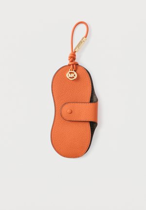 Orange textured leather eyeglass case with a snap closure, gold circular MK logo charm, and matching looped wrist strap on a white background.