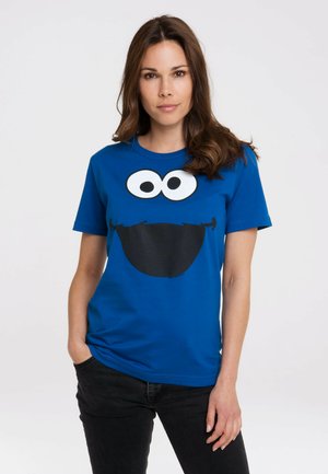 Blue cotton t-shirt featuring a large graphic of Cookie Monster’s face, with two white eyes and a black mouth area. Short sleeves and crew neckline.